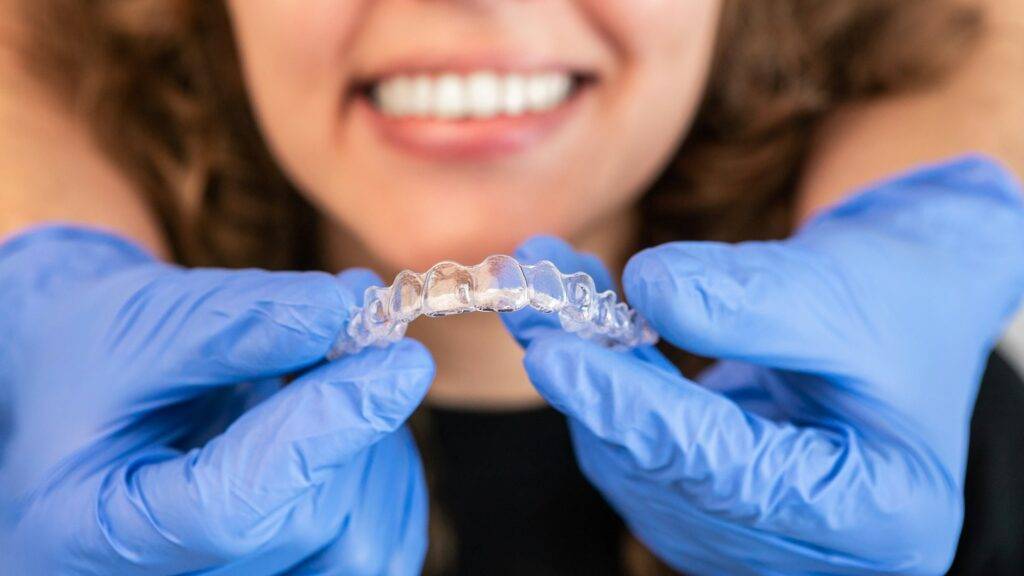Orthodontist doctor putting silicone invisible transparent braces on woman teeth